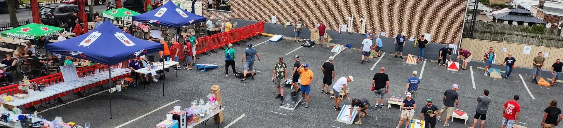 A top down view of the event, including the cornhole boards, prizes table, and a crowd of others.